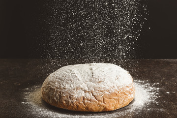 Sprinkling of flour onto fresh bread against dark background