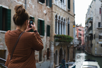 Fototapeta na wymiar Beautiful girl traveler photographs the streets and canals of Venice on her smartphone.