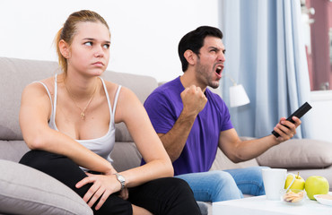 Disappointed girl on sofa while man watching tv