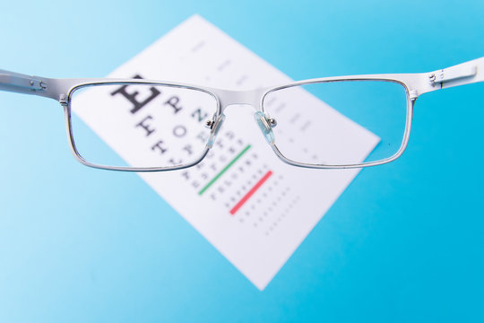 Hand-held White glasses, view of the Snellen chart. Blue background