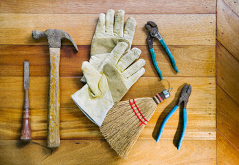 Collection of various old rusty tools with leather work gloves and hand broom arranged on wood bench surface
