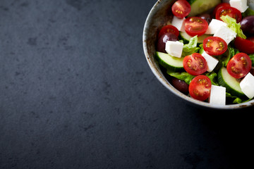Salad with Kalamata Olives, Cucumber Cherry Tomatoes and Feta Cheese on black Stone Background. Healthy Snack Idea. Close up.