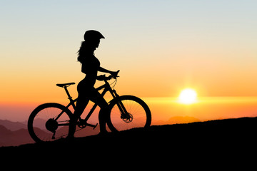 Girl on a mountain bike on offroad, beautiful portrait of a cyclist at sunset, Fitness girl rides a modern carbon fiber mountain bike in sportswear, a helmet, glasses and gloves..