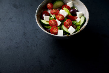 Salad with Kalamata Olives, Cucumber Cherry Tomatoes and Feta Cheese on black Stone Background. Healthy Snack Idea. Close up.