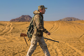 A hunter in camouflage and a gun in his hands in the early morning on top of a mountain stands looking for a target. Beautiful mountain landscape, the opening of the hunt.