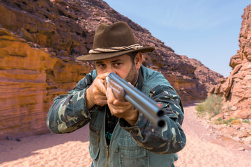 A hunter in camouflage and a gun in his hands in the early morning on top of a mountain stands...