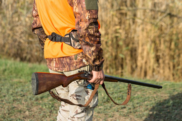 A man with a gun in his hands and an orange vest on a pheasant hunt in a wooded area in cloudy...