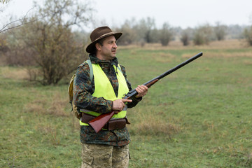 Hunting period, autumn season open. A hunter with a gun in his hands in hunting clothes in the autumn forest in search of a trophy. A man stands with weapons and hunting dogs tracking down the game.