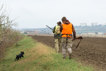 A mans with a gun in his hands and an orange vest on a pheasant hunt in a wooded area in cloudy...