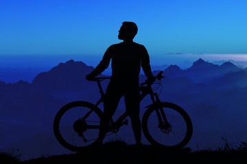 Obraz premium Cyclist in shorts and jersey on a modern carbon hardtail bike with an air suspension fork rides off-road on the orange-red hills at sunset evening in summer..