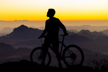 Cyclist in shorts and jersey on a modern carbon hardtail bike with an air suspension fork rides off-road on the orange-red hills at sunset evening in summer..