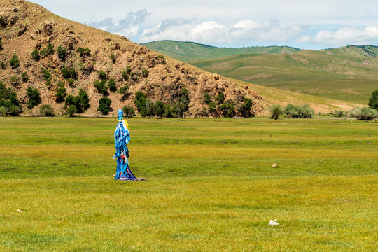 Small Mongolian Ovoo (Ceremonial Rock Pile with Silk Scarves) on grassy meadow near mountains, Mongolia.