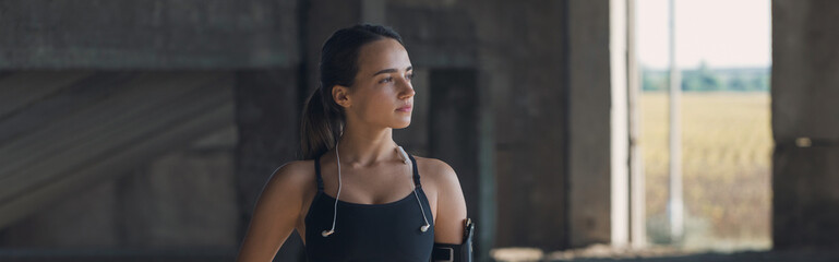 A thin athletic girl takes a break between classes on the background of the building in the early morning, enjoys silence and freedom. Panoramic image, toned.