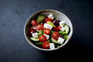 Fototapeta na wymiar Salad with Kalamata Olives, Cucumber Cherry Tomatoes and Feta Cheese on black Stone Background. Healthy Snack Idea. Copy space. 