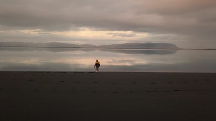 Girl in winter jacket writing on black sand on beach at sunset,