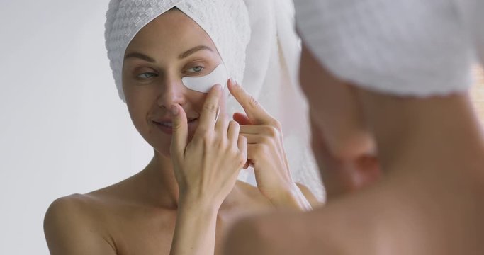 Happy 30s woman apply eye patches looking in bathroom mirror