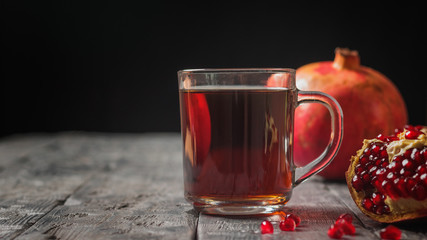 Glass mug with pomegranate juice and fresh pomegranates on a wooden table.