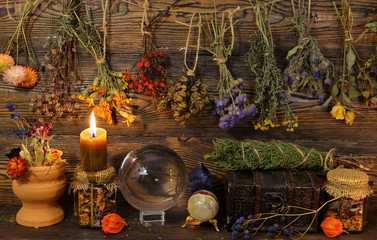 Still life with dry herbs, crystal ball, bottle and burning candle on witch table.