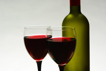 Two glasses with red wine and a green bottle on gray
