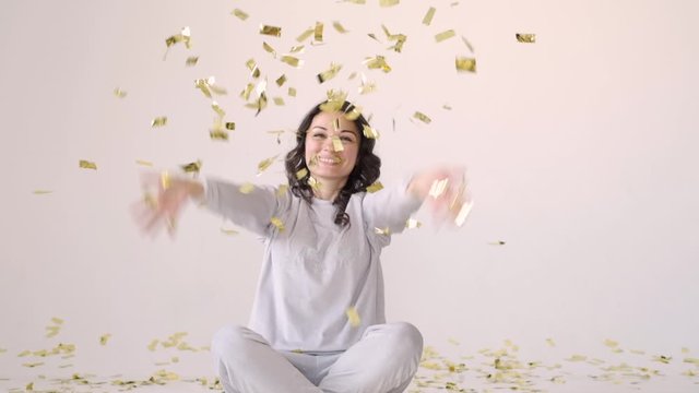 A woman celebrates, rejoices in the rain from the candy. Success, party, celebration concept.Young girl dancing and having fun in the rain of confetti on a white background.