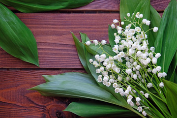 Lily of the valley bouquet and leaves on a wooden background
