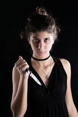 Obraz premium Teenager girl threateningly holds a small knife in his hand. Concept of protection against domestic violence. On a black background.