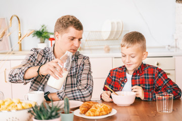 Obraz na płótnie Canvas Young father with an 8-year-old son in a checkered shirt have breakfast in the kitchen, time together, family relationship, one parent concept