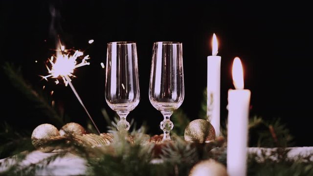 Two glasses with champagne with christmas decor, sparkler background and candles