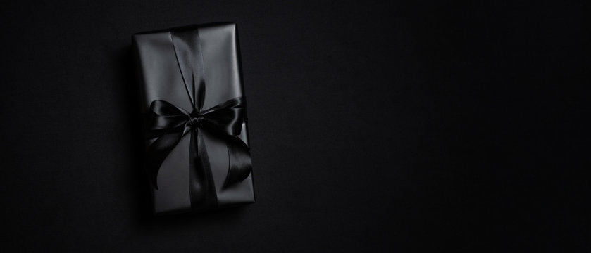 Top view of black gift box with black ribbons isolated on black background.