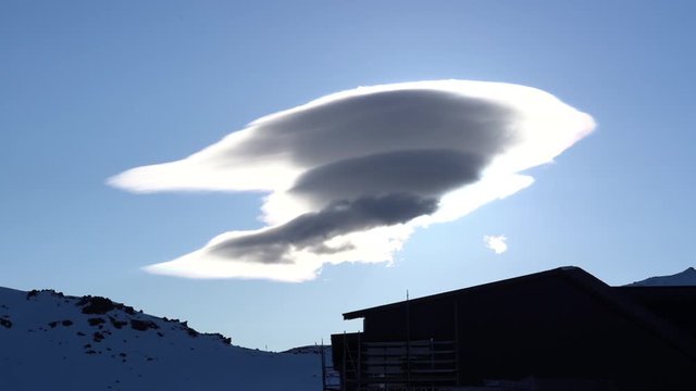 Timelapse of a lenticular cloud morphing and dissolving over a building on a mountain