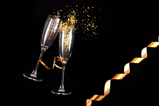 Two champagne glasses with golden sparkles over black background. Happy new year.