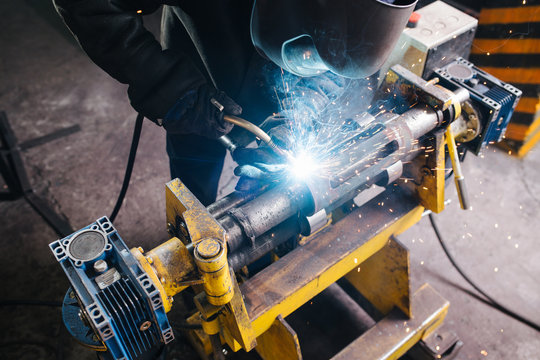 Hish angle image of a welder working on metal piece, fixed with industrial clamp