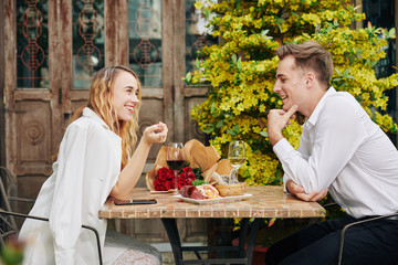 Happy young couple flirting, drinking wine and eating snacks at restaurant table