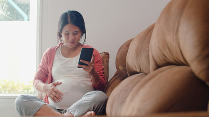 Young Asian Pregnant woman using mobile phone search pregnancy information. Mom feeling happy...