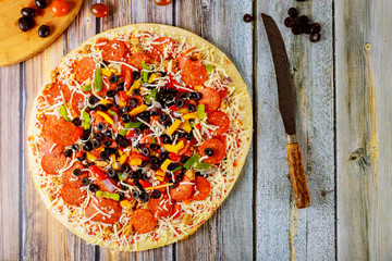 Delicious supreme pizza on wooden table with knife and olives.