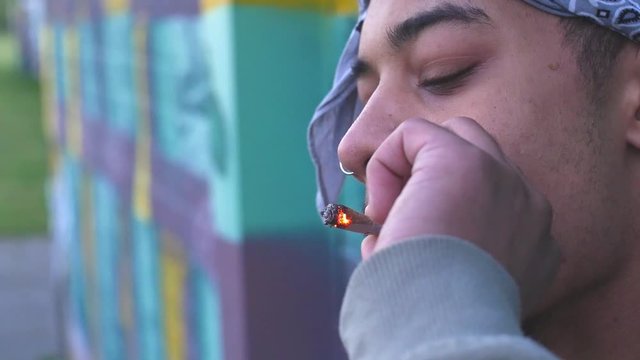 dolly shot of a young colored guy in a gray hoodie with two chains around his neck smoking a joint