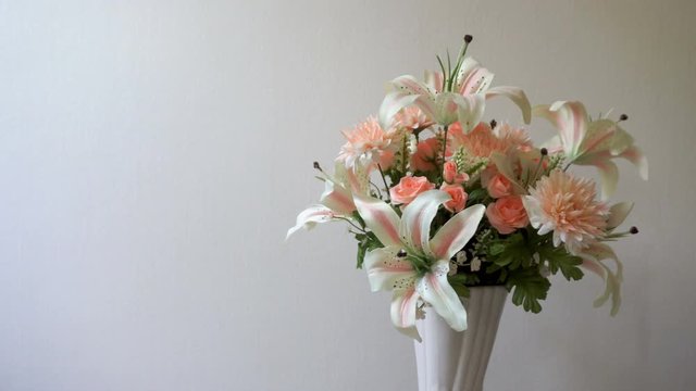 Lilies, roses, carnations flowers in pink vase on white background is rotating. Pastel flower collection presentation
