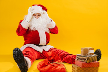 Santa Claus sitting on the floor with his legs apart, tired of packing presents