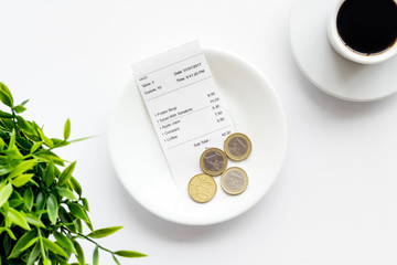Pay restaurant bill by cash. Reciept and coins on plate on white background top view