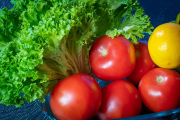 Vegetable still life on a dark background. Tomatoes, lettuce and lemon. Vegetarianism. Recipes of vegetable dishes. A raw food diet. Wholesome food. Daily consumption of vegetables.