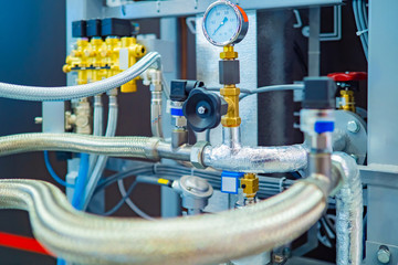 Flexible pipes in a metal braid. Pressure gauge and valves on the pipes. Industrial concept. Fragment of the industrial apparatus. Gas compressor. The production of liquefied natural gas.