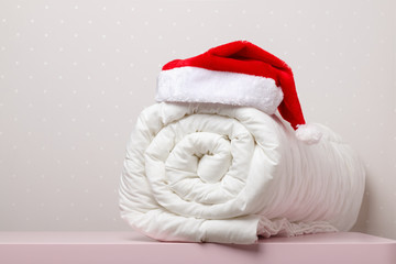 Close-up of white warm duvet roll with a cap of Santa Claus on the table against the background of...