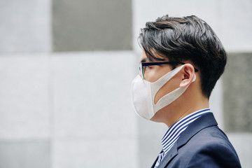 Side view of serious Asian man wearing protective mask due to air pollution in the city