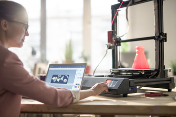 Creative female designer pushing button on control panel of 3d printer