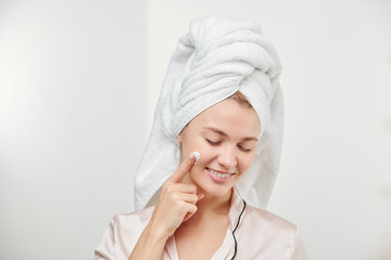 Pretty young satisfied woman applying hydrating cream on her face