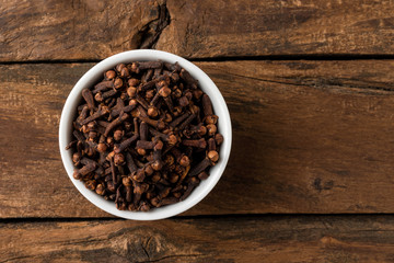 Cloves in bowl on rustic wooden table. Top view