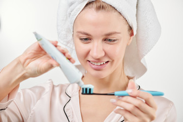 Healthy young woman applying toothpaste on toothbrush before brushing teeth