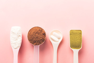 Various collagen powder types on pink background. Plain, matcha, chocolate and pills. Flat lay, top...