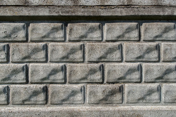 A fragment of gray concrete relief wall or fence imitating several rows of rectangular bricks laid horizontally. Abstract architectural or industrial background