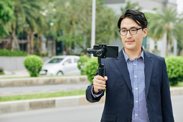 Asian man in glasses making video on smartphone attached to monopod